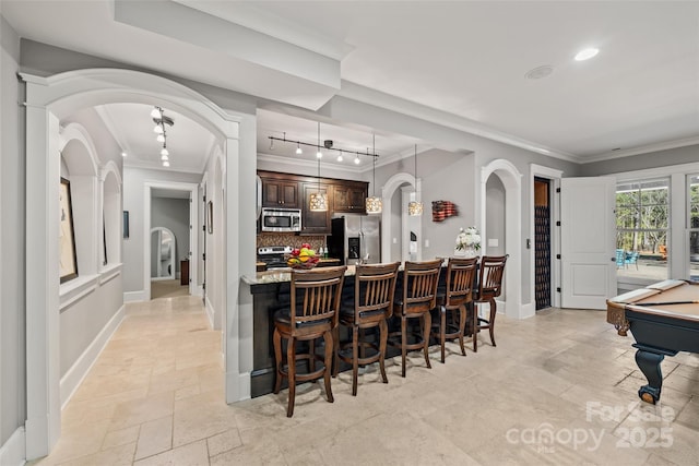 kitchen featuring appliances with stainless steel finishes, a breakfast bar, billiards, tasteful backsplash, and dark brown cabinets