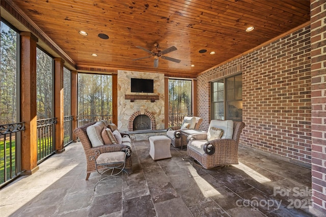 unfurnished sunroom with an outdoor stone fireplace, wood ceiling, and ceiling fan