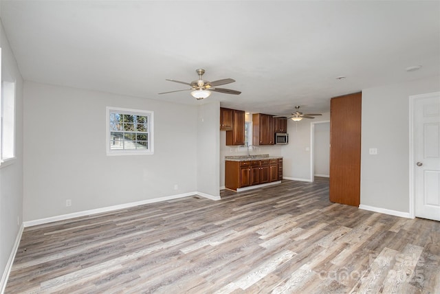 unfurnished living room featuring light wood-type flooring, ceiling fan, and sink