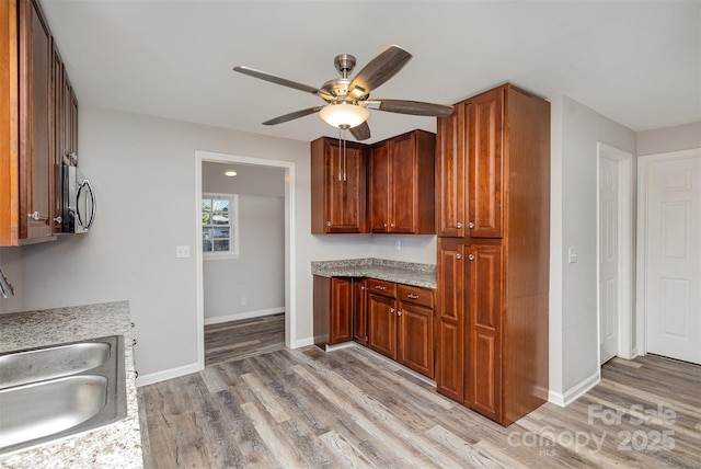 kitchen with ceiling fan, light wood-type flooring, sink, and light stone counters