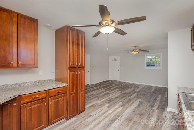 kitchen with ceiling fan, sink, light stone counters, and light hardwood / wood-style flooring