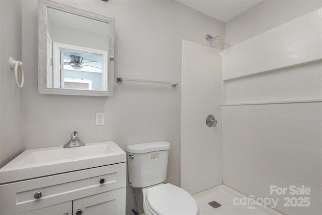 bathroom featuring ceiling fan, toilet, tiled shower, and vanity