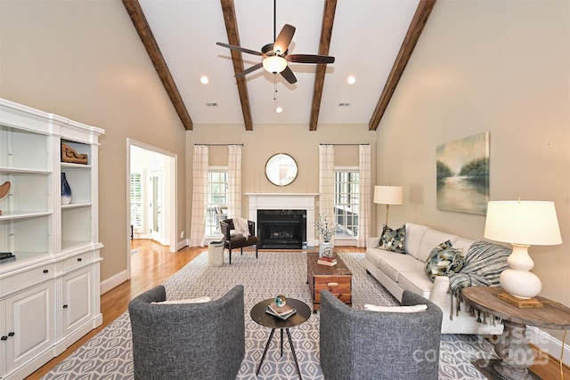 living room with a high end fireplace, vaulted ceiling with beams, light hardwood / wood-style flooring, and ceiling fan