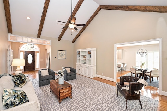 living room with plenty of natural light, ceiling fan with notable chandelier, high vaulted ceiling, and light hardwood / wood-style flooring