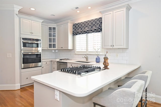 kitchen with kitchen peninsula, appliances with stainless steel finishes, decorative backsplash, sink, and white cabinets