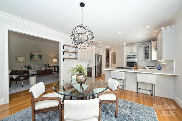 dining area with light hardwood / wood-style flooring, an inviting chandelier, beverage cooler, and ornamental molding