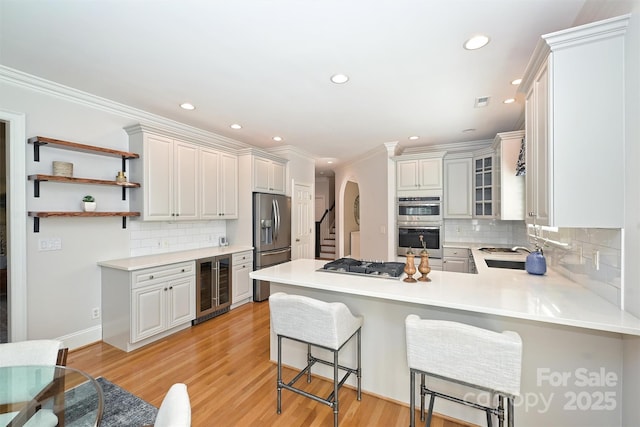 kitchen featuring kitchen peninsula, ornamental molding, a breakfast bar, beverage cooler, and white cabinets