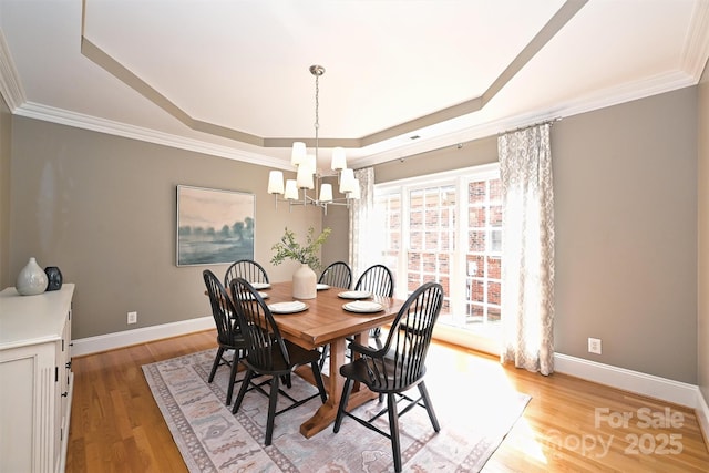 dining area featuring a tray ceiling, a chandelier, light hardwood / wood-style floors, and ornamental molding