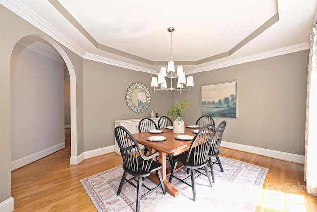 dining space with an inviting chandelier, light wood-type flooring, ornamental molding, and a tray ceiling