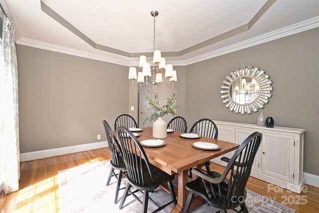 dining space with a tray ceiling, an inviting chandelier, ornamental molding, and light hardwood / wood-style floors