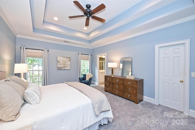 carpeted bedroom featuring a raised ceiling, ensuite bath, ceiling fan, and crown molding