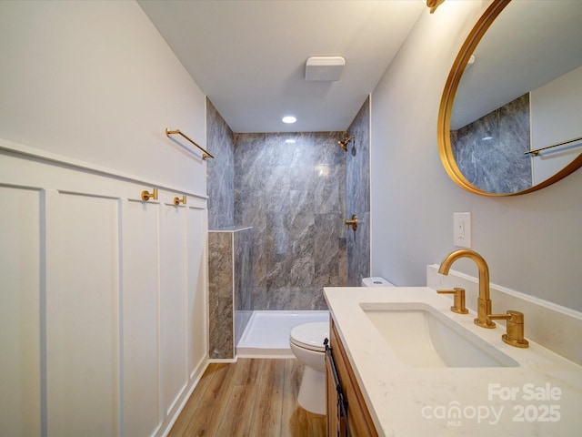 bathroom with a tile shower, vanity, wood-type flooring, and toilet