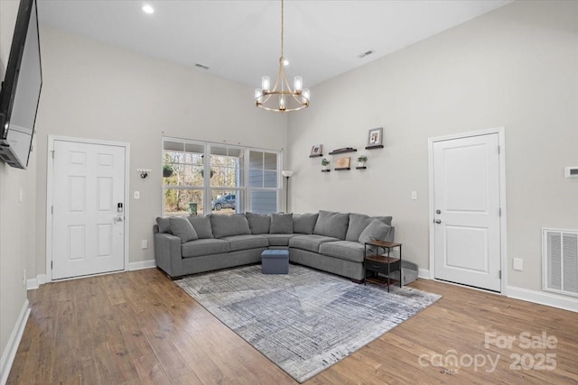 living room with light hardwood / wood-style flooring, a towering ceiling, and an inviting chandelier