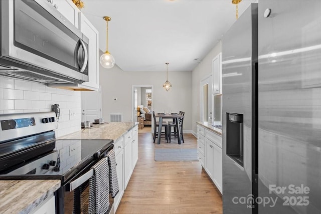 kitchen with white cabinets, stainless steel appliances, light stone counters, and decorative light fixtures