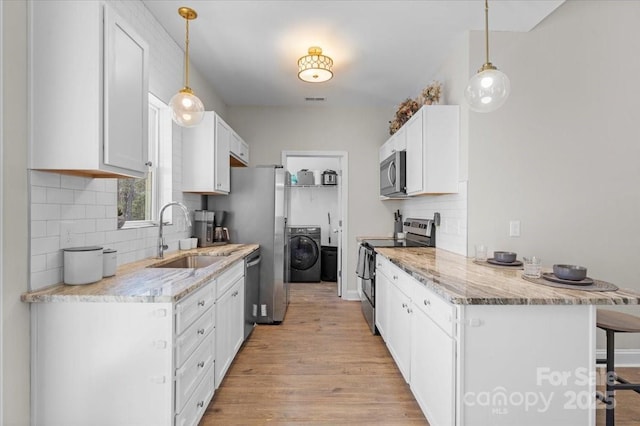 kitchen with pendant lighting, washer / clothes dryer, white cabinetry, stainless steel appliances, and sink