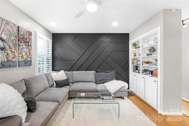 living room featuring built in shelves, light hardwood / wood-style flooring, and ceiling fan