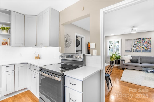 kitchen with light hardwood / wood-style floors, electric stove, stacked washer / dryer, and tasteful backsplash