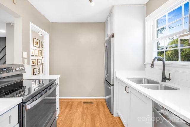 kitchen with appliances with stainless steel finishes, light hardwood / wood-style floors, white cabinetry, and sink