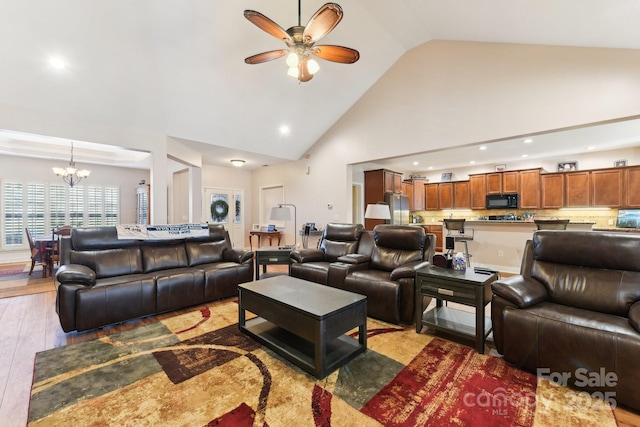 living room featuring ceiling fan with notable chandelier, high vaulted ceiling, and light wood-type flooring