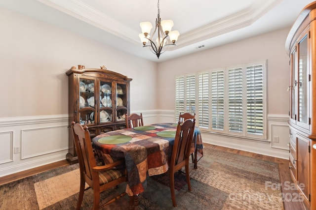 dining room with crown molding, a tray ceiling, dark wood-type flooring, and a chandelier