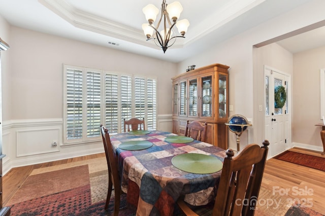 dining room with a raised ceiling, a chandelier, and light hardwood / wood-style floors