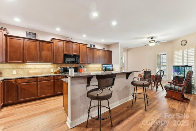 kitchen with dark stone counters, an island with sink, a breakfast bar area, and stove