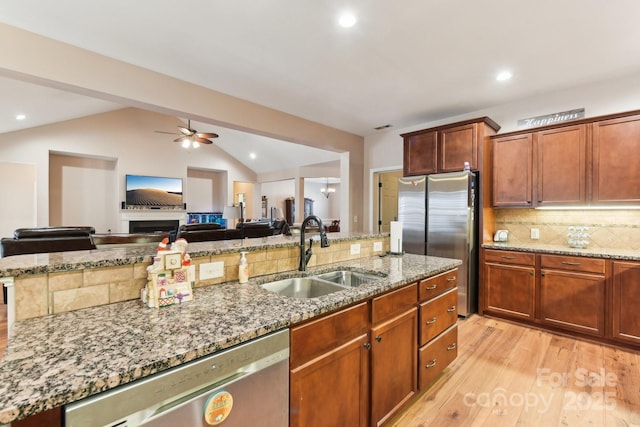 kitchen with lofted ceiling, sink, stainless steel appliances, light stone countertops, and light hardwood / wood-style floors