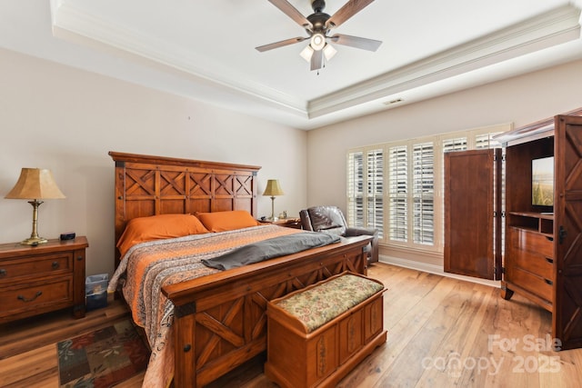 bedroom featuring crown molding, ceiling fan, a tray ceiling, and light wood-type flooring