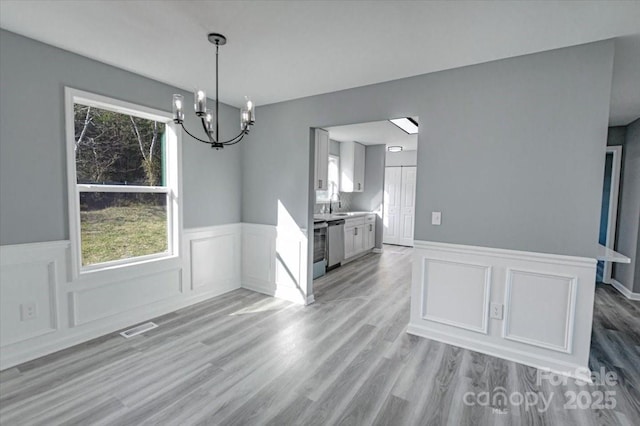 unfurnished dining area featuring sink, light hardwood / wood-style flooring, and an inviting chandelier