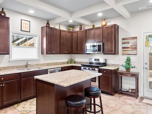 kitchen featuring beam ceiling, sink, stainless steel appliances, a breakfast bar, and a kitchen island