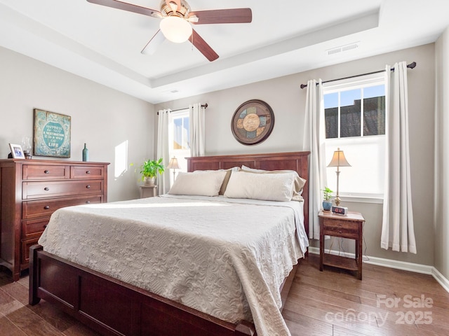 bedroom featuring ceiling fan, dark hardwood / wood-style floors, and a tray ceiling