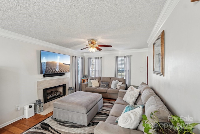 living room with ceiling fan, wood-type flooring, a textured ceiling, a tiled fireplace, and ornamental molding