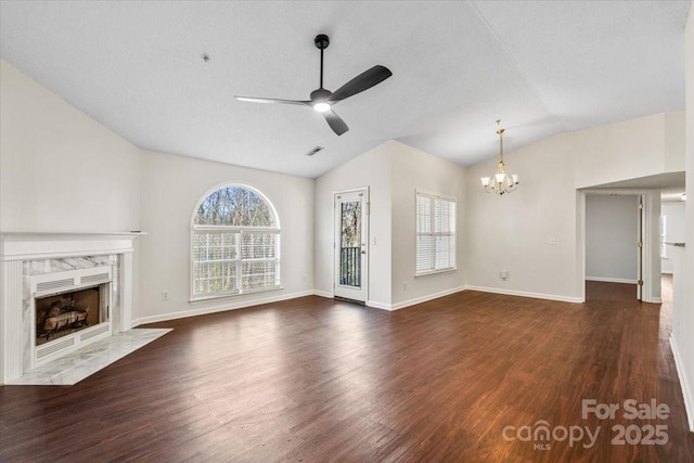 unfurnished living room with dark hardwood / wood-style flooring, ceiling fan with notable chandelier, vaulted ceiling, a healthy amount of sunlight, and a premium fireplace