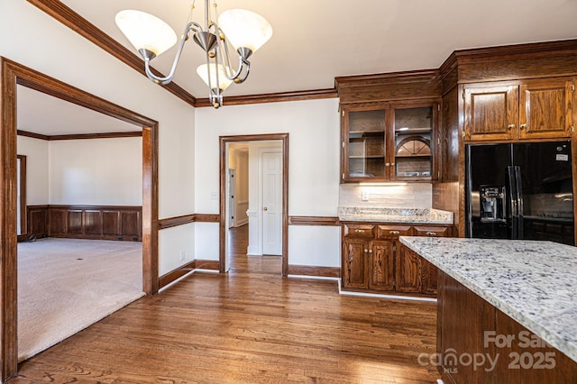 kitchen with black refrigerator with ice dispenser, crown molding, hanging light fixtures, light stone countertops, and a chandelier