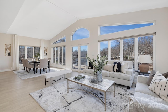 living room with high vaulted ceiling, french doors, and light hardwood / wood-style flooring