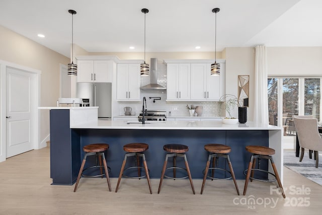 kitchen featuring white cabinetry, high quality fridge, pendant lighting, wall chimney range hood, and a breakfast bar