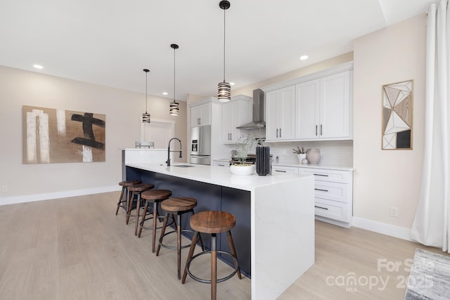 kitchen featuring white cabinets, a large island with sink, hanging light fixtures, wall chimney range hood, and a breakfast bar