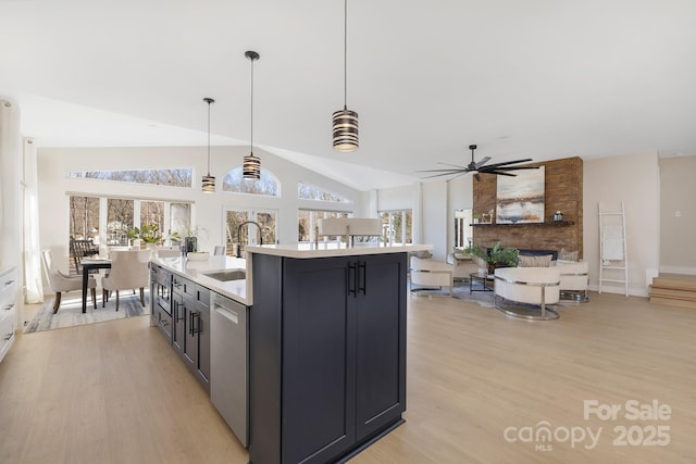 kitchen featuring hanging light fixtures, lofted ceiling, light wood-type flooring, a kitchen island with sink, and sink