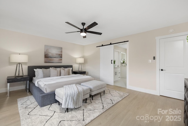 bedroom featuring ensuite bath, light wood-type flooring, ceiling fan, and a barn door