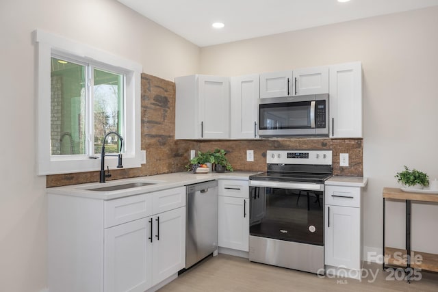 kitchen featuring tasteful backsplash, light wood-type flooring, white cabinets, appliances with stainless steel finishes, and sink