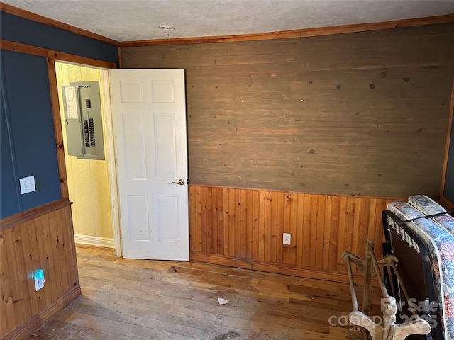 empty room featuring hardwood / wood-style flooring, wood walls, crown molding, and electric panel