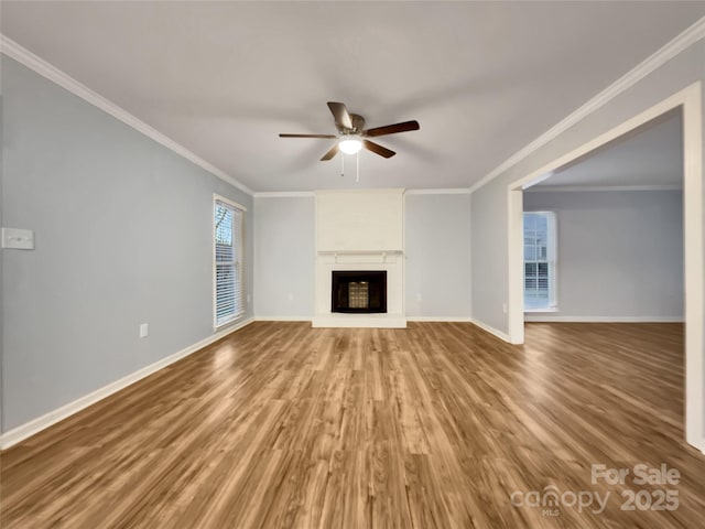 unfurnished living room featuring ceiling fan, a large fireplace, crown molding, and hardwood / wood-style flooring