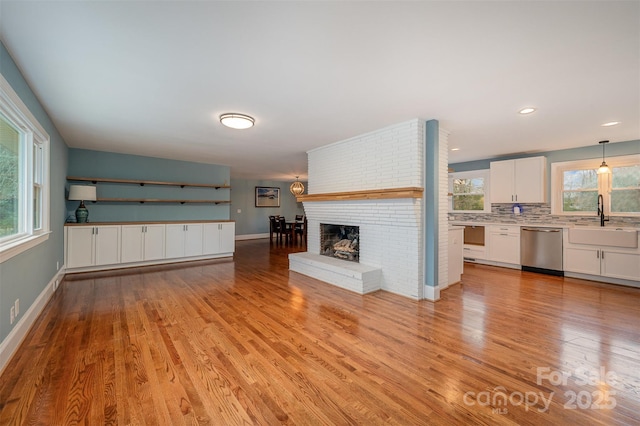 unfurnished living room with sink, a healthy amount of sunlight, light wood-type flooring, and a brick fireplace