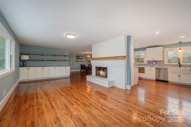 unfurnished living room featuring sink, a brick fireplace, a wealth of natural light, and light hardwood / wood-style flooring