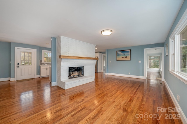 unfurnished living room with a brick fireplace, light wood-type flooring, and a wealth of natural light