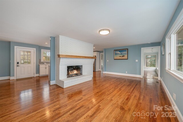 unfurnished living room featuring a brick fireplace, light wood-type flooring, and a healthy amount of sunlight