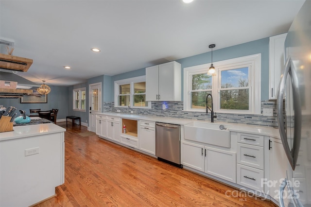 kitchen with pendant lighting, light hardwood / wood-style floors, white cabinetry, appliances with stainless steel finishes, and sink