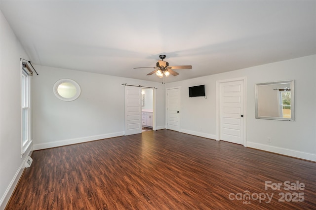 spare room with ceiling fan, dark hardwood / wood-style flooring, and a barn door