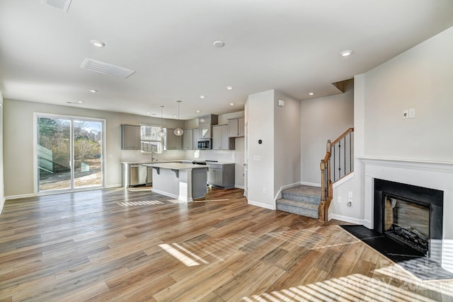 kitchen with light hardwood / wood-style floors, pendant lighting, a center island, gray cabinets, and a breakfast bar area