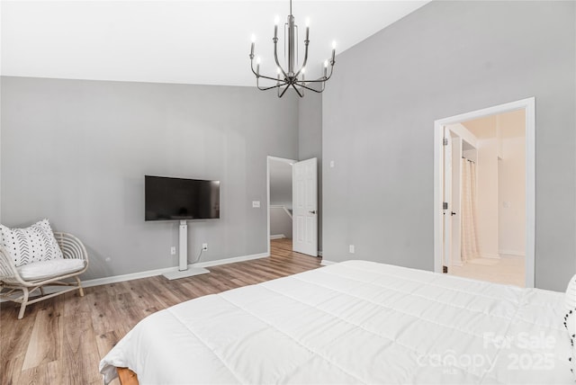 bedroom with connected bathroom, hardwood / wood-style floors, high vaulted ceiling, and a notable chandelier